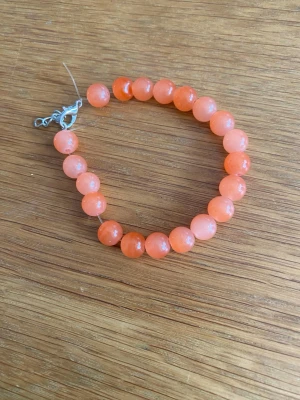 Orange pärlarmband med metallås - Snyggt armband med runda, orange pärlor i glas eller sten och ett enkelt metallås. Pärlorna har en glansig finish och armbandet ger en fräsch och färgstark vibe till din outfit. Perfekt för dig som vill ha något som sticker ut lite extra.