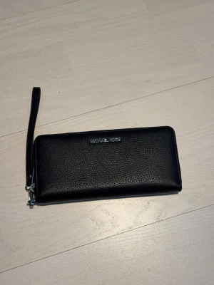 Plånbok Michael Kors - Elegant svart plånbok från Michael Kors i läder, aldrig använt! Gott om plats för kort, sedlar och mynt, plus avtagbar handledsrem. Nypris på Zalando: 1995kr Kan gärna gå ner i pris då den aldrig har blivit använt och förtjänar ett bättre hem med uppskattning!❤️🥲