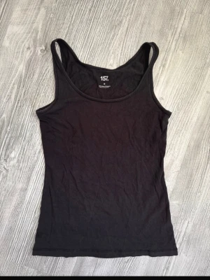 Svart linne från Lager 157 Medium - En enkel och stilren svart linne från Lager157. Toppen har smala axelband och är tillverkad i mjuk bomull med lite stretch för en bekväm passform. Perfekt att matcha med jeans eller kjol för en clean look.