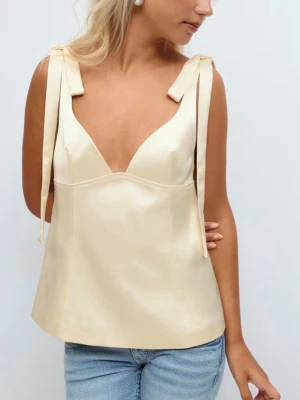 Pastellgul satinlinnetopp med knyt - Snygg pastelgul topp i satin med breda axelband som knyts till rosetter. Toppen har en v-ringad urringning. Perfekt att styla med jeans eller kjol för en somrig outfit. Den är endast provad och därmed aldrig använd. Pris kan diskuteras!💛