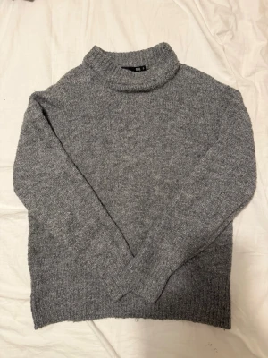 Grå stickad tröja med polokrage - Mysig grå stickad tröja från lager157. Tröjan har en rak passform och är tillverkad i ett mjukt, melerat garn som ger en avslappnad look. Perfekt för kyliga dagar och enkel att matcha med jeans eller kjol.