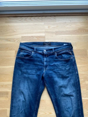 Blå jeans från Replay - Snygga blå jeans från Replay med klassisk femficksmodell och raka ben. Jeansen har en mörk tvätt med lätt slitning och kontrastsömmar. Tillverkade i bomull med en skön stretch för extra komfort!!