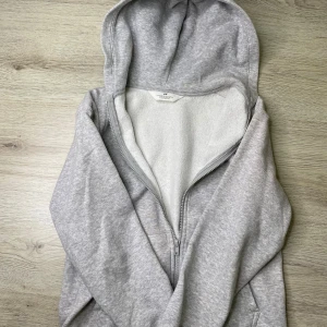 Ljusgrå zip hoodie från H&M - Ljusgrå hoodie från H&M med dragkedja framtill och mjuk, fleecefodrad insida. Klassisk huva och två fickor på sidorna. Perfekt för en avslappnad och bekväm stil. Tillverkad i bomullsblandning för extra komfort.