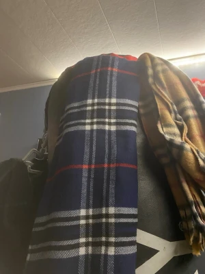 Mörkblå och beige rutiga halsdukar  - Två halsdukar i klassiskt rutigt mönster. En i mörkblått med vita och röda ränder, och en i beige med svarta och röda detaljer. Perfekta för att addera lite stil till din outfit. Mjukt material som känns skönt runt halsen.