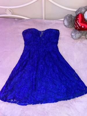 Blå spetsklänning från NLY Blush - Snygg blå axelbandslös kortklänning från NLY Blush i spets. Klänningen har en feminin passform med lätt utställd kjol och vacker spetsdetalj över hela plagget. FINNS PÅ FLER SIDOR!!