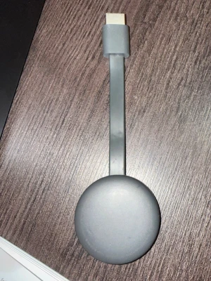 Google Chromecast grå HDMI-enhet - Smidig och stilren Google Chromecast i matt grå plast. Rund form med platt HDMI-kabel, perfekt för att streama innehåll till din TV. Enkel att koppla in och använda med olika streamingtjänster. Passar alla som vill göra sin TV smartare.