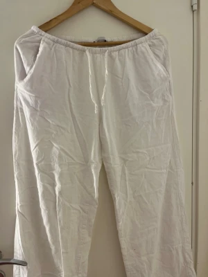 Vita linnebyxor med resårmidja - Säljer ett par vita linnebyxor med avslappnad passform och resår i midjan. Byxorna har raka ben och sidofickor, perfekta för en chill och luftig stil. Materialet är linne som ger en skön känsla och andas bra under varma dagar.