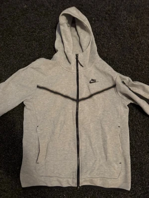 Grå Nike Tech -  klassisk grå Nike Tech. Riktigt stilren och passar bra med de flesta plaggen.