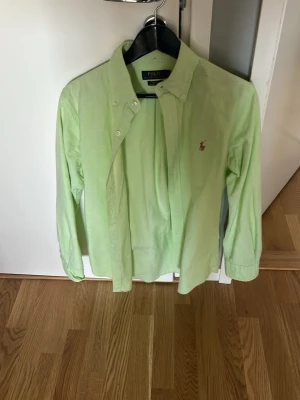Ljusgrön skjorta från Polo Ralph Lauren - Snygg ljusgrön skjorta från Polo Ralph Lauren med klassisk button-down krage och broderad logga på bröstet. Skjortan har långa ärmar och knappar framtill. Perfekt för en clean och stilren look.