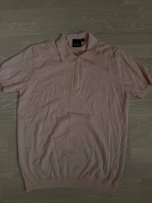 Ljusrosa polotopp med dragkedja - Snygg ljusrosa polotopp från Oscar Jacobson med kort ärm och dragkedja framtill. Toppen har klassisk krage och är tillverkad i mjukt bomullsmaterial. Perfekt för en stilren och avslappnad look.