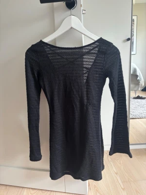 Svart strandklänning med knytning - Snygg svart strand klänning i transparent virkat material med långa ärmar knytning i ryggen. Säljer då den aldrig kom till användning 