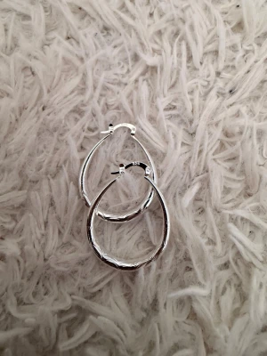 Silvriga S925 örhängen i oregelbunden form  - Säljer ett par stilrena örhängen i äkta silver med oregelbunden, organisk form. De är blanka och har en enkel klickstängning. Perfekta för dig som gillar minimalistiska smycken med en twist.