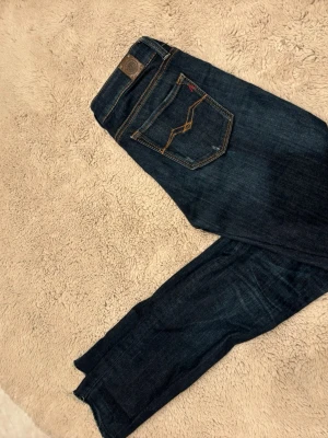 Mörkblå skinny jeans från Replay - Snygga mörkblå skinny jeans från Replay med klassiska fem fickor och kontrastsömmar. Jeansen har en låg midja och smal passform, samt detaljerad bakficka med gul söm. Tillverkade i mjukt denimtyg för en bekväm känsla.