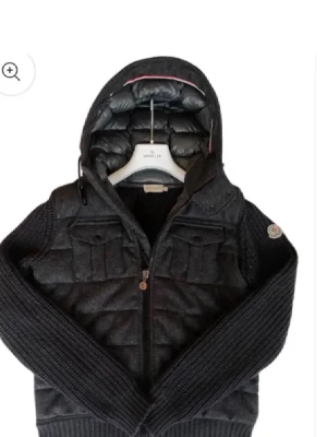 Moncler Tricot cardigan  - Snygg mörkgrå jacka från Moncler med stickade ärmar och quiltad kropp. Jackan har huva, två bröstfickor med lock och dragkedja framtill. Perfekt för dig som vill ha en sportig men ändå stilren look.
