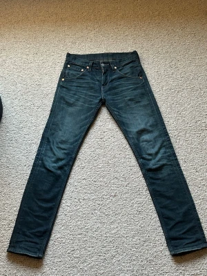 Mörkblå Levi's slim fit jeans - Säljer ett par mörkblå slim fit jeans från Levi's med klassisk femficksdesign och snygg tvätt framtill. Jeansen har en patch bak i midjan och en ficka med knappdetalj. Perfekta för dig som gillar en smalare passform och tidlös stil.