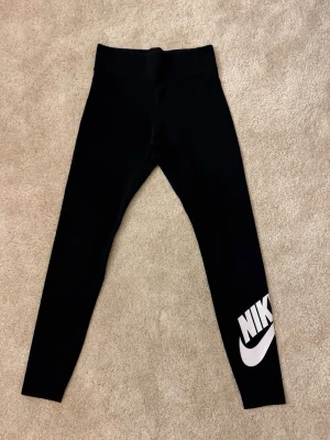 Svarta tights från Nike - Säljer ett par svarta tights från Nike. De har hög midja och är tillverkade i stretchigt material som sitter tight. Perfekta för träning eller chill. Klassisk och sportig look. (Är i mer tyg material än träningsmatrial)