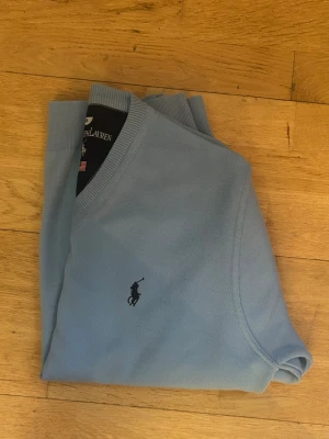 Ljusblå tröja från Polo Ralph Lauren - Ljusblå långärmad tröja från Polo Ralph Lauren med klassisk v-ringning. Liten missfärgning/fläck fram (zooma in bild 2) som mest troligt går bort i tvätt/med borttagningsmedel. Annars otroligt fint skick. Storlek M hyfsat liten i storlek.