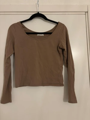 Brun långärmad topp från Gina Tricot - En basic brun långärmad topp från lindex med rundad halsringning och croppad passform. Tillverkad i mjuk bomullsmix som är skön mot huden. Perfekt att styla med jeans eller kjol för en enkel och snygg look.