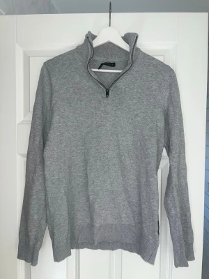 Grå stickad tröja med halv dragkedja - Snygg grå stickad tröja från french conection med hög krage och halv dragkedja. Tröjan har ribbade muddar vid ärmslut och nederkant, perfekt för lager på lager. Enkel och stilren design som passar till det mesta.