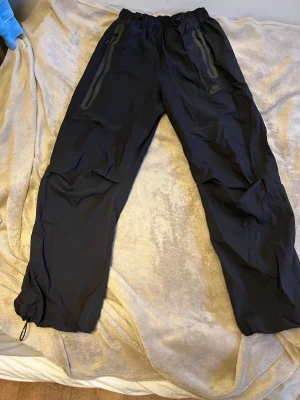 Svarta Nike tech track pants oanvända! Oversize XS - Hej! Säljer dessa Nike tech track pants byxor helt oanvända! Dem är oversize och är i storlek xs men jag är 183 och de sitter ganska baggy dom kostar 1249 i butik jag säljer för 950 då de är helt oanvända.