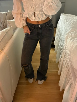 Svarta raka jeans Gina Tricot  - Säljer ett par svarta raka jeans med slitningar på knät och fransiga benslut. Jeansen har klassisk femficksmodell och hög midja. Perfekta för en avslappnad och trendig look. Materialet är denim i bomull.