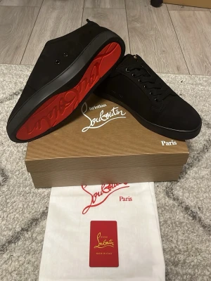 Louboutin skor - Snygga svarta sneakers från Christian Louboutin med ikonisk röd sula. Skorna har en stilren design i mocka och läder, svarta skosnören och diskreta detaljer. Perfekta för dig som vill sticka ut med exklusiva och trendiga sneakers. Om du har några frågor eller om du vill ha mer bilder är det bara att skriva till mig.