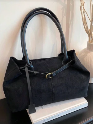 Svart handväska i mocka-look - Stilren svart handväska i mocka-liknande material med dubbla handtag i slätt läder och dekorativt spänne framtill. Väskan har en mjuk, rektangulär form och minimalistisk design som passar till många outfits.