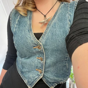 Jeansväst från Zara - Säljer en klassisk blå jeansväst från Zara med v-ringning och tre knappar framtill. Västen har en figurnära passform och är perfekt att styla över en t-shirt eller klänning för en cool look.