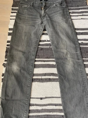 Gråa jeans från J.Lindeberg - Snygga gråa jeans från J.Lindeberg med klassisk femficksmodell och dragkedjegylf. Jeansen har en tvättad look med ljusa slitningar och raka ben. Perfekta för en avslappnad och trendig stil.