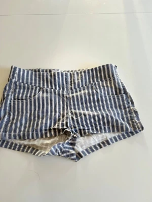 Randiga blåvita shorts i bomull - Snygga blå och vita shorts med vertikala ränder och två framfickor. De har en klassisk passform och är tillverkade i mjuk bomull, perfekta för varma dagar. Shortsen har även en bakficka och bred linning för extra komfort. PASSAR ÄVEN FOLK SOM HAR S