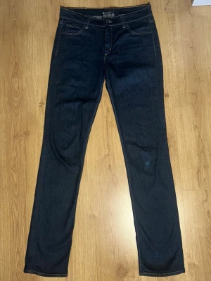 Mörkblå Acne slim jeans - Snygga mörkblå jeans från Acne med slim/rak passform och fem fickor. Jeansen har kontrastsömmar och en läderpatch med logga bak i midjan. Tillverkade i slitstark denim som ger en tidlös look. Storlek 33/34 men titta på måtten.
