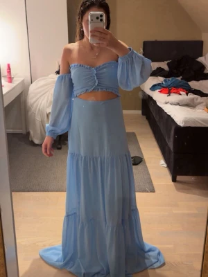 Blå långklänning med offshoulder - Säljer en ljusblå långklänning med offshoulder och puffiga ärmar. Skulle ha denna till min bal 2025 men den kom inte till användning då jag valde en annan. Den är ny med prislapp och allt kvar, den är köpt för 1200kr
