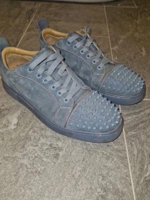 Blåa sneakers med nitar - Unika blå sneakers i mocka med matchande blåa nitar på tån och ovansidan. Skorna har gråblå snören och en låg siluett. Insidan är beige och sulan är i samma blå ton som ovandelen. Perfekta för dig som vill sticka ut med din stil.