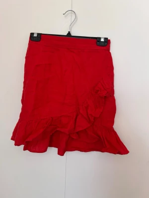 Röd volangkjol i linne i storlek XS(34) - Snygg röd kortkjol med volangdetaljer och omlottkänsla. Kjolen har en feminin och lekfull design som passar perfekt till varmare dagar. Tillverkad i ett lätt och luftigt linnematerial som ger en skön känsla.Mycket fint skick,sparsamt använd i några få tillfällen 