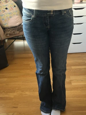 Blå bootcut jeans med broderade fickor - Säljer ett par blå bootcut jeans från 157 med snygga broderade detaljer på bakfickorna. Jeansen har normalhög/låg midja, klassisk femficksmodell och stängs med dubbla knappar och dragkedja. Perfekta för dig som gillar en avslappnad men ändå trendig look. Är slitna vid fötterna