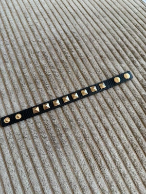Svart läderarmband med nitar - Snyggt svart armband i läder med guldiga fyrkantiga nitar och tryckknappar. Perfekt accessoar för en edgy look och passar till många olika stilar.
