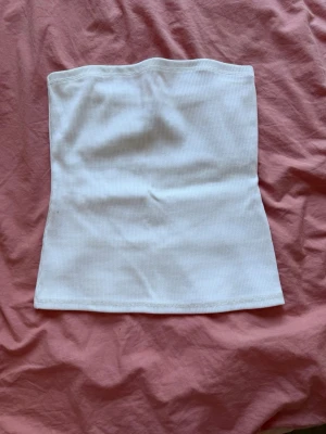 Vit ribbad tubtopp från Weekday - En stilren vit ribbad tubtopp i stretchigt material. Toppen är axelbandslös och har en enkel, rak passform som passar perfekt till många olika outfits. Knappt använd