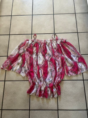 Rosa och vit blus med leopardmönster storlek L/XL - Säljer en luftig blus från Rita Fasion  med rosa och vita partier samt leopardmönster och kedjedetaljer. Blusen har offshoulder-modell med resår upptill och nertill samt vida ärmar. Perfekt för dig som gillar färg och mönster.