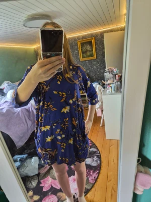 Blommig blå klänning från Indiska - Snygg blå kortklänning från Indiska med gult och vitt blommönster. Klänningen har trekvartsärm och en loose passform som ger en avslappnad look. Perfekt för dig som gillar färg och mönster!