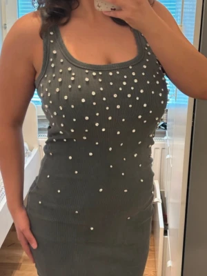 Grå ribbad klänning med pärlor - Snygg grå ribbad klänning med pärldetaljer framtill. Ärmlös modell med rund halsringning och tight passform. Perfekt för dig som vill sticka ut med en unik och trendig look.