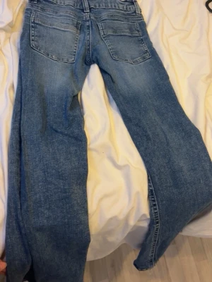 Blå bootcut jeans med slitningar - Snygga blå bootcut jeans med klassisk femficksdesign och dragkedja. Jeansen har en tvättad look med slitningar och är tillverkade i denim. Perfekta för en avslappnad och trendig stil.