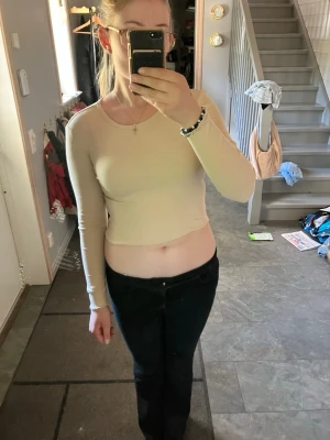 Beige croppad långärmad topp - Trendig beige croppad topp med lång ärm och rund halsringning. Sitter tight och är perfekt att styla med höga jeans eller kjol. Enkel och stilren design som passar till många olika looks.