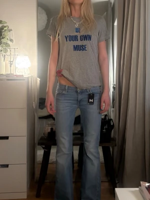 Grå t-shirt med blå text - Säljer en grå t-shirt med trycket 'BE YOUR OWN MUSE' i blå bokstäver. T-shirten har korta ärmar, rund halsringning och en avslappnad passform. Perfekt till jeans eller shorts för en chill look.