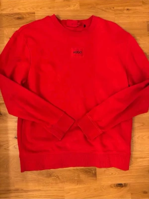 Röd sweatshirt från Hugo - Riktigt snygg röd sweatshirt från Hugo med diskret logga på bröstet. Tröjan har rund halsringning, långa ärmar och ribbade muddar vid ärmslut och nederkant. Perfekt för en avslappnad och trendig look.