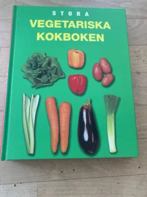 Stora Vegetariska Kokboken - En färgglad och inspirerande kokbok med grön pärm och bilder på olika grönsaker på framsidan. Perfekt för dig som vill laga vegetariska rätter och få nya idéer till köket. Innehåller recept, tips och näringsinformation.