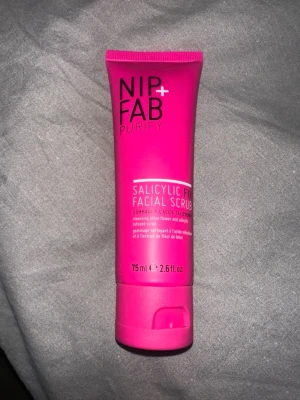 NIP+FAB Salicylic Fix Facial Scrub - En ansiktsskrubb från NIP+FAB i en starkt rosa tub på 75 ml. Produkten innehåller salicylsyra och lotusblomma, perfekt för djuprengöring av huden. Tuben är gjord av plast och har en praktisk skruvkork.