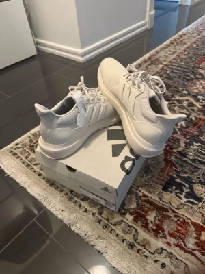 Adidas ultras boost - Snygga grå vita  sneakers från Adidas ultras boost  med klassiska tre ränder på sidan. Ovandelen är i ventilerande meshmaterial och sulan är tjock och bekväm. Perfekta för dig som gillar stilrena och sportiga skor. Skorna har snörning och en modern, clean look.