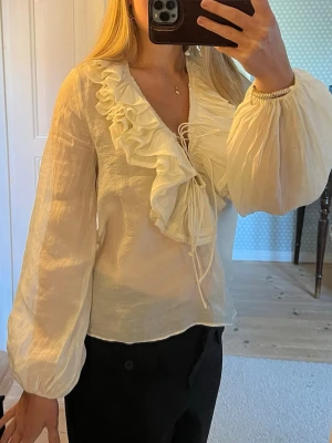 Romantisk blus med volang och knytning - Supersöt vit blus med stora volanger längs v-ringningen och knytning framtill. Den har lite små röda märken men dem är under kragen så dem syns inte. Har även ett märke på ärmen (se bild) men det är inte heller någon man lägger märke till💓❣️ 
