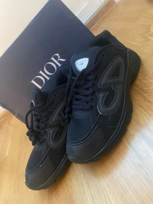 Svarta  sneakers med mesh och läder - Snygga svarta sneakers  med coola detaljer i både mesh och läder. Skorna har en chunky sula, svarta skosnören och en tydlig CD-logga på plösen. Perfekta för dig som gillar streetstyle och exklusiva märken.