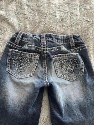 Blå jeans med broderade bakfickor - Snygga blå jeans från Gina Tricot med broderade detaljer på bakfickorna och kontrastsömmar i vitt och rött. Väldigt bra sick då de har blivit för stora! 
